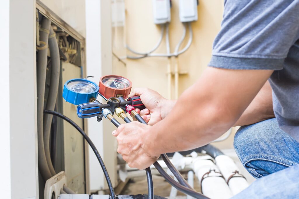 Air repair mechanic using measuring equipment for filling industrial factory air conditioners.